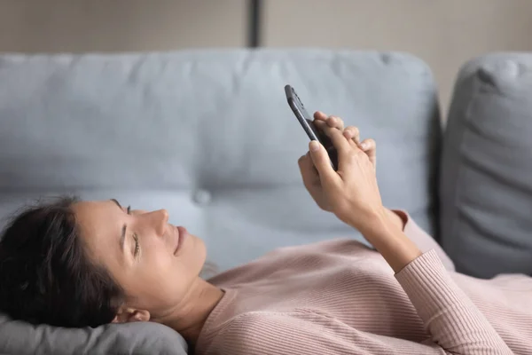 Mujer joven y bonita tumbada en el sofá con gadget smartphone — Foto de Stock