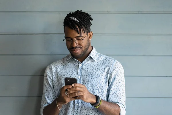 Happy handsome millennial African guy texting message on mobile phone — Stock Photo, Image