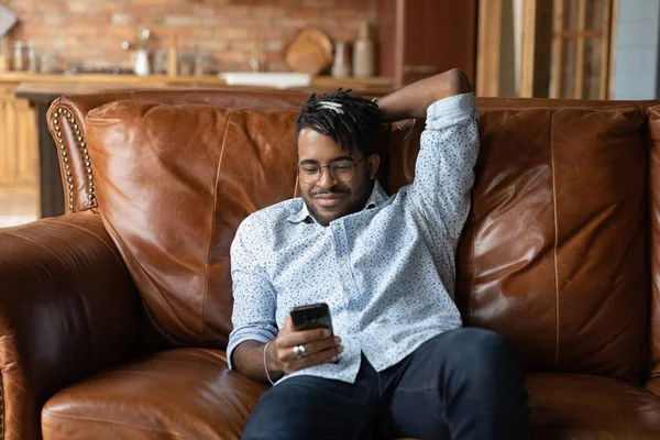 Happy lazy African American guy using smartphone — Stock Photo, Image