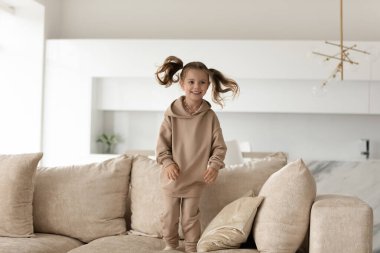 Mutlu heyecanlı küçük kız yumuşak koltukta zıplıyor