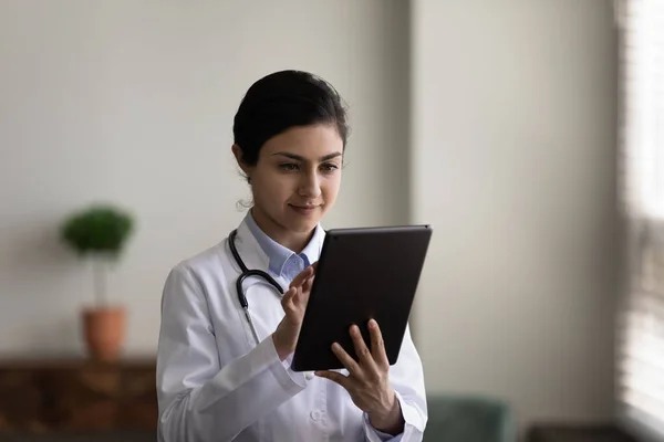Concentrated young indian female doctor using digital tablet.
