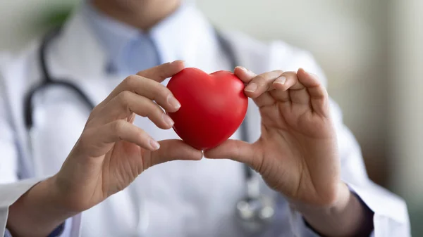 Close up young female doctor holding heart figure in hands.