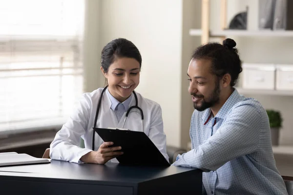 Jovem médico indiano feliz discutindo o tratamento com paciente africano. — Fotografia de Stock