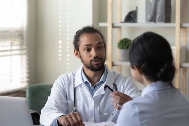 Konsantre genç Afrikalı Amerikalı doktor Hintli hastaya danışmanlık yapıyor..