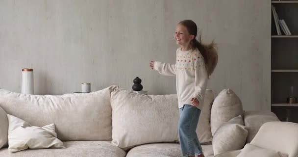 Активная беззаботная маленькая девочка прыгает на мягком диване дома — стоковое видео
