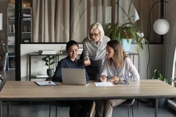 Mature businesswoman mentor training diverse interns, pointing at laptop screen — Stock Photo, Image