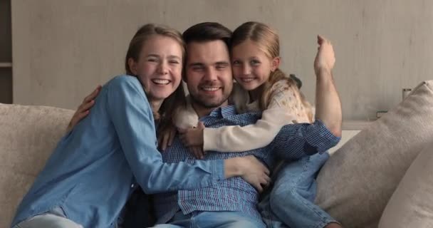 O familie fericită stă pe canapea îmbrățișându-se zâmbind uitându-se la cameră — Videoclip de stoc