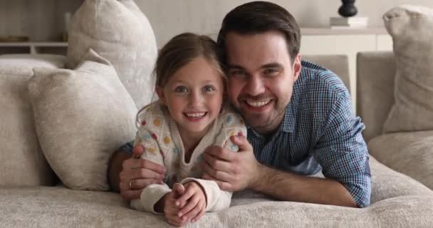 Padre cariñoso abrazando a la hija acostada en el sofá mira la cámara — Vídeo de stock