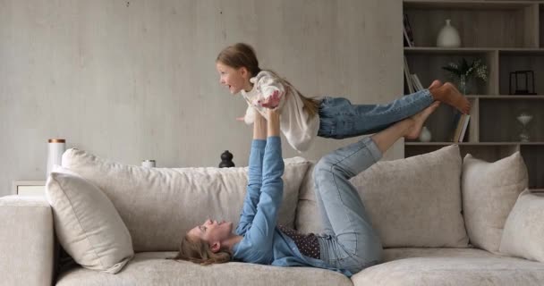 Madre cariñosa acostada en el sofá elevadores en las manos hija — Vídeo de stock