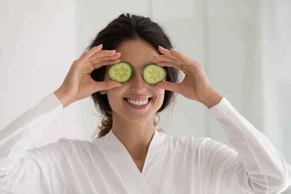 Sonriente joven latina sosteniendo rodajas de pepino en los ojos. — Foto de Stock