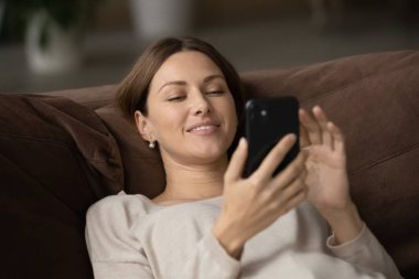 Akıllı telefon kullanan, kanepede dinlenen, gülümseyen kadını kapat.