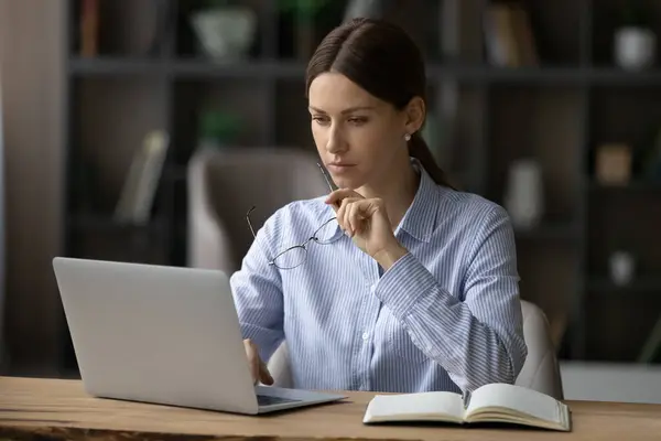 Mujer reflexiva confiada mirando la pantalla del ordenador portátil, trabajando en el proyecto — Foto de Stock