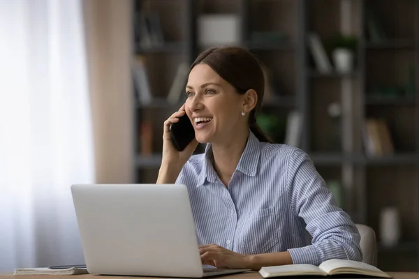 Femme d'affaires excitée parlant au téléphone, assise au bureau avec un ordinateur portable — Photo