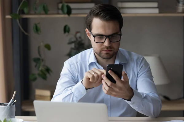 Hombre de negocios enfocado usando teléfono inteligente en el lugar de trabajo, lectura de mensajes de texto — Foto de Stock