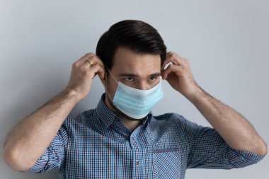 Ciddi 30 'lu yaşlardaki genç bir adam tıbbi maske takıyor.