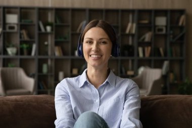 Kanepede oturan kulaklıklı, gülümseyen bir kadının portresi.