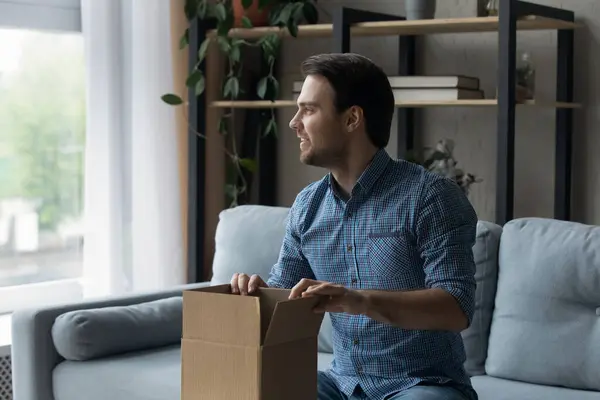 Happy excited millennial guy unpacking carton box at home