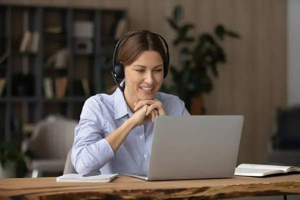 Усміхнена бізнес-леді в навушниках говорить, дивлячись на екран ноутбука — стокове фото