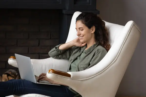 Uśmiechnięta młoda kobieta korzystająca z komputera, odpoczywająca w domu. — Zdjęcie stockowe