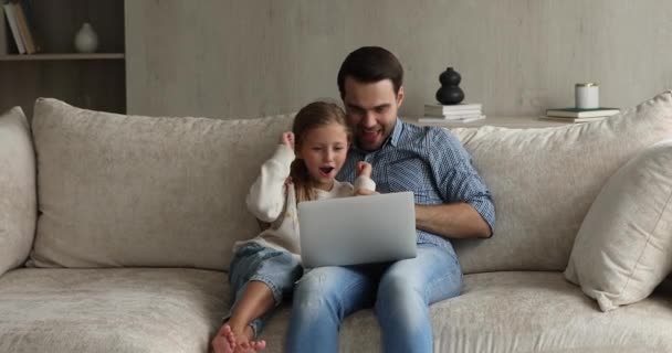 Padre e figlia si siedono sul divano a guardare cartoni animati sul computer portatile — Video Stock