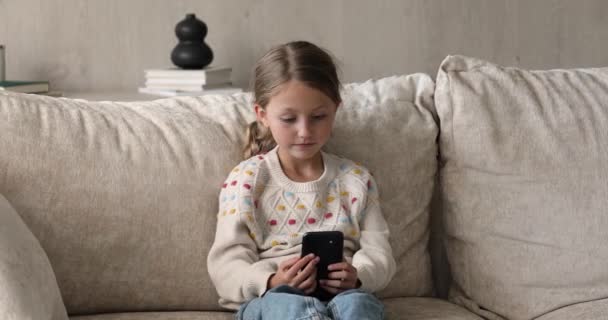 Cute little girl sit alone on sofa with smartphone — Stock Video