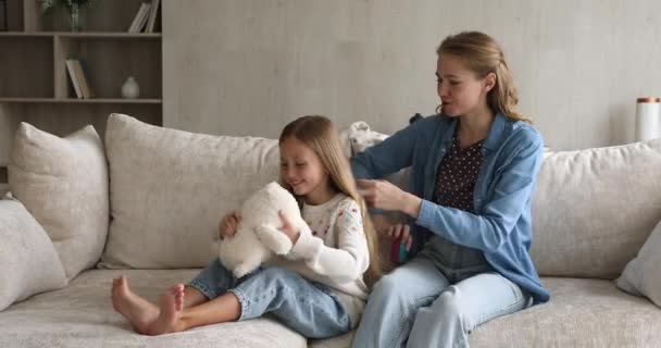 Любящая мать расчесывает длинные светлые волосы маленькой милой дочери — стоковое видео