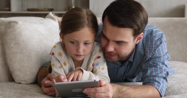 Baba ve tatlı kız dijital tabletle kanepede dinleniyorlar. — Stok video