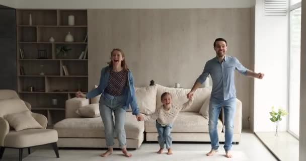 Família de mãos dadas pulando dançando na acolhedora sala de estar — Vídeo de Stock