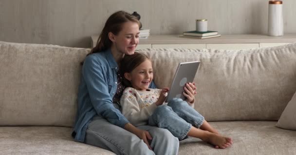 Niña y madre se sientan en el sofá con la tableta digital — Vídeo de stock