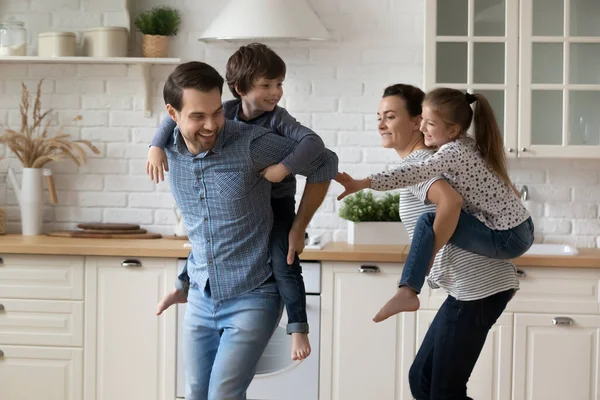 Excited active parents piggybacking sibling kids, chasing each other — Stock Photo, Image