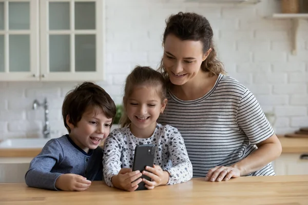 Glückliche Mutter und zwei Kinder, die gemeinsam das Handy benutzen und Freude empfinden — Stockfoto