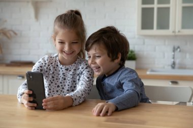 Mutlu erkek ve kız kardeşler cep telefonu kullanıyor ve eğleniyorlar.