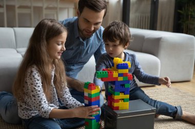 Baba oğluna ve kızına bloklardan kule yapmayı öğretiyor.