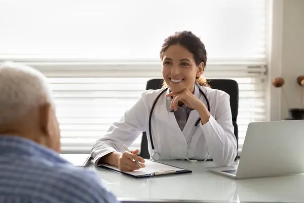 Happy optimistic female doctor in white coat giving consultation — Stock Photo, Image