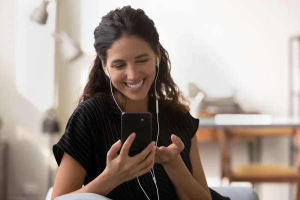 Happy Latin woman in earphones talking on cellphone — Stock Photo, Image