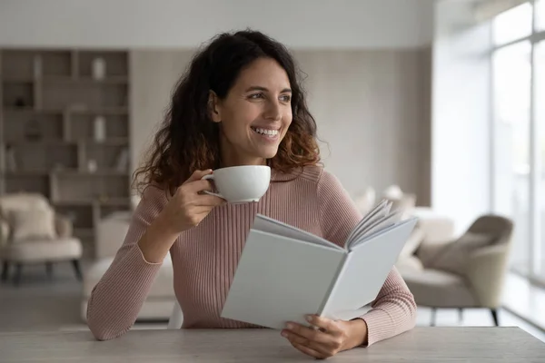 Happy young hispanic woman reading book and drinking coffee. — Stock Photo, Image