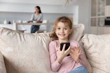 Anne mutfakta otururken küçük kız telefonda oynuyor..