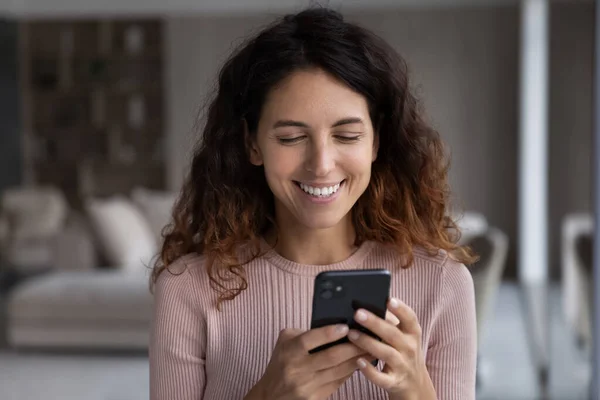 Glimlachende jonge Spaanse vrouw leest aangename boodschap op mobiele telefoon. — Stockfoto