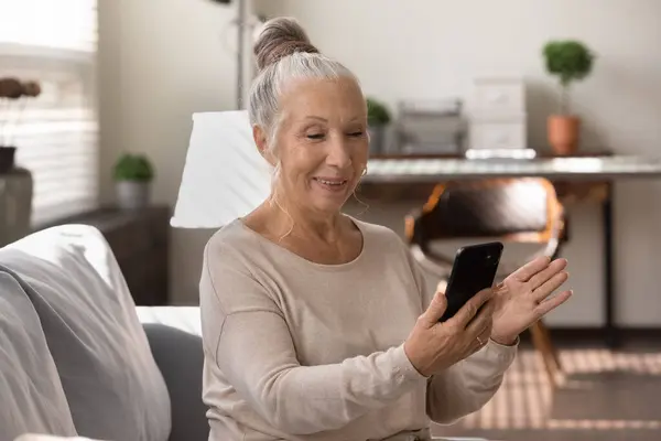 Счастливая пожилая женщина использует смартфон дома, делает видеозвонок — стоковое фото