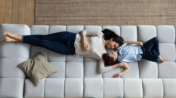 Friedliche junge koreanische asiatische Mutter ruht sich auf Sofa mit Kind aus. — Stockfoto