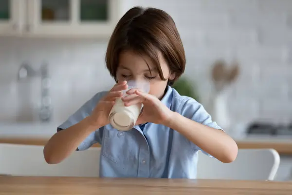 Głodny uroczy mały chłopiec pijący szklankę świeżego jogurtu. — Zdjęcie stockowe