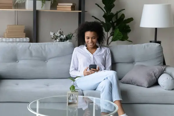 Calma preto adolescente feminino relaxar no sofá macio usando smartphone — Fotografia de Stock