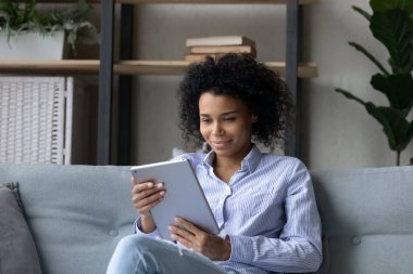 Gülümseyen Afrikalı kadın kanepeye oturur ve elektronik tablet kullanır.