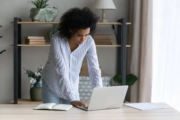 Задумчивая черная женщина стоит за столом размышляя над электронным документом — стоковое фото