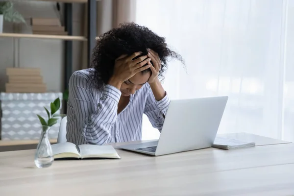 Depressive schwarze Frau sitzt am Arbeitsplatz und umarmt Kopf — Stockfoto