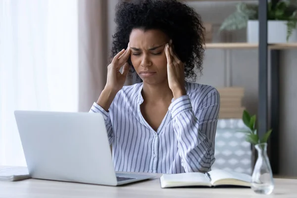 Exhausted overworked african american woman sit by laptop rub temples — Stock Photo, Image