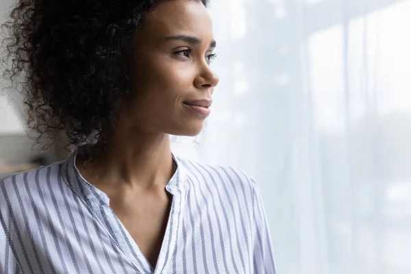 Wanita hitam milenial yang percaya diri berdiri oleh jendela melihat ke depan memvisualisasikan — Stok Foto
