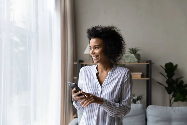 Joyeux jeune femme noire en utilisant le téléphone près de la fenêtre — Photo