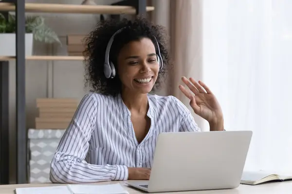 Mujer birracial de confianza en la mano de onda de auriculares a la pantalla del ordenador portátil —  Fotos de Stock