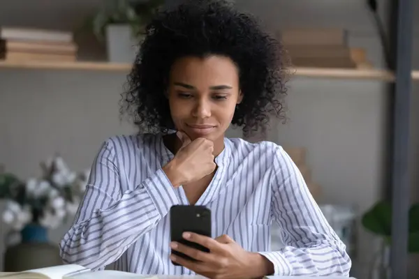 Молодая женщина смешанной расы думать на информацию на экране телефона — стоковое фото